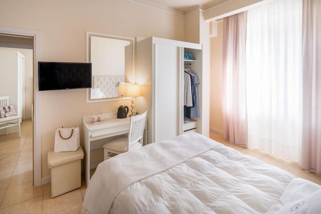 Une chambre d’hôtel équipée d’un lit, d’un bureau, d’une chaise, d’une télévision, d’une armoire et d’une fenêtre avec des rideaux.