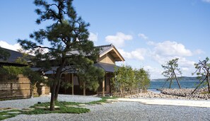 Une maison traditionnelle japonaise avec une allée en gravier, entourée de pins et offrant une vue sur la mer.