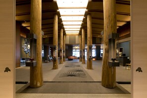 A spacious lobby with high wooden pillars, a central seating area, and a modern design.