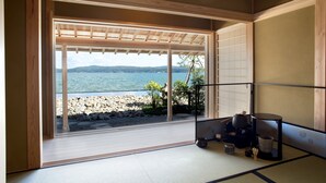 Ein Zimmer mit Blick auf einen felsigen Strand und das Wasser, mit Tatami-Böden und traditioneller japanischer Einrichtung.