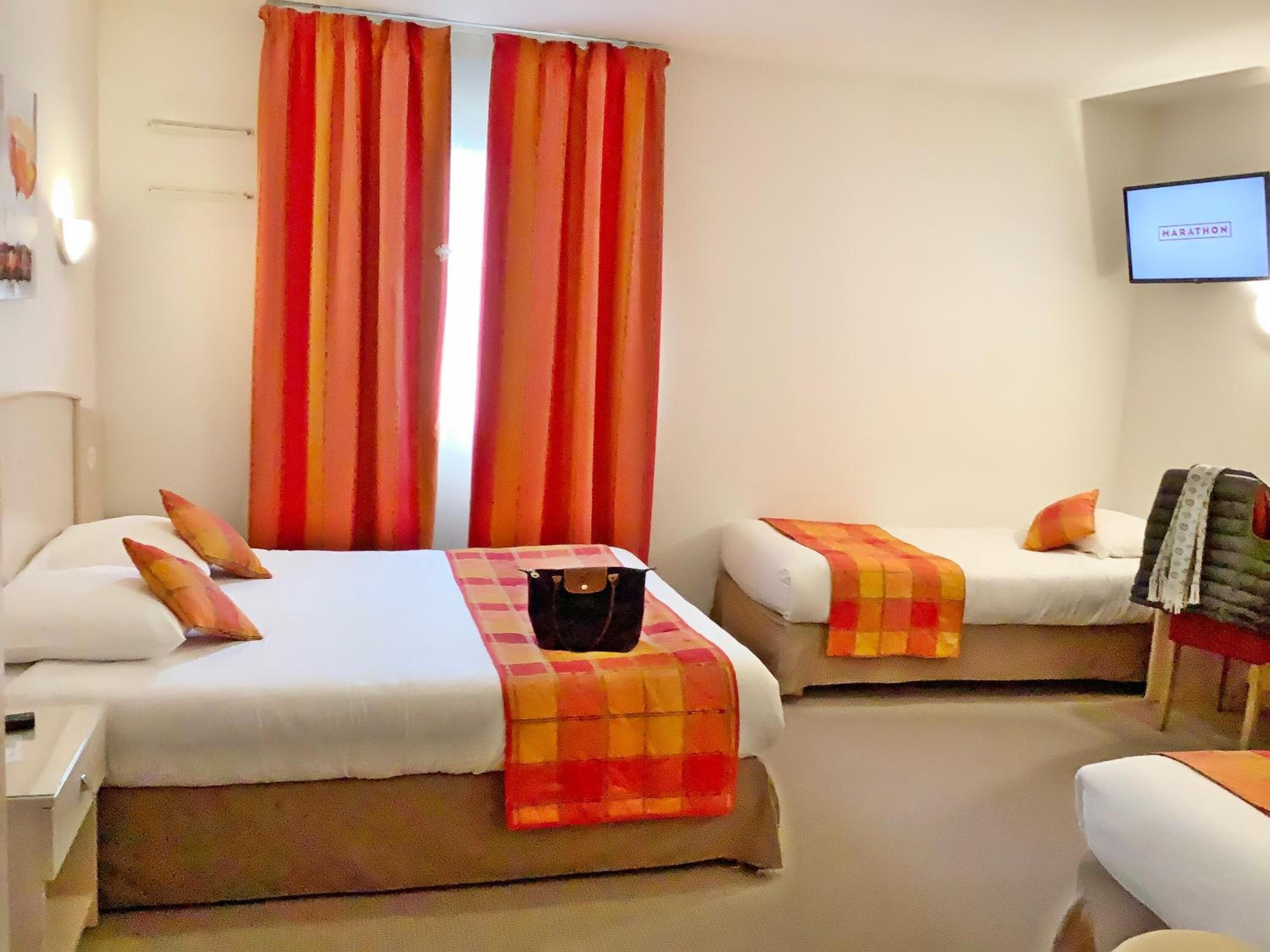A hotel room with two beds, each with a checkered blanket and pillows. There is a television on the wall and a suitcase on one of the beds.