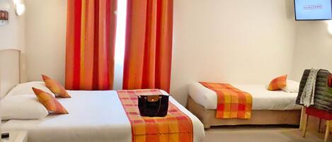 A hotel room with two beds, each with a checkered blanket and pillows. There is a television on the wall and a suitcase on one of the beds.