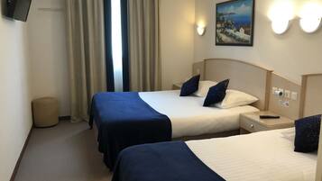 Ein Hotelzimmer mit zwei Betten, einem an der Wand montierten Fernseher, einem Gemälde und einem Nachttisch mit Fernbedienung.