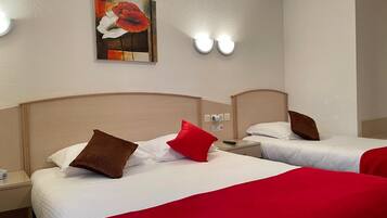A hotel room with two beds, each with white bedding and red accents. There is a painting on the wall above the beds, and a nightstand with a remote control and a lamp.