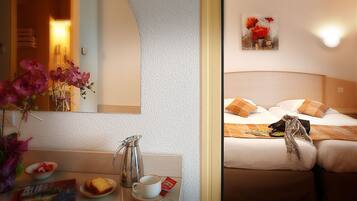 Ein Hotelzimmer mit einem Bett, Kissen, einer Kaffeemaschine, einer Tasse und einem Blumenstrauß.