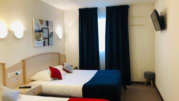 Habitación de hotel con dos camas, un televisor de pantalla plana montado en la pared, un cuadro sobre las camas y una ventana con cortinas oscuras.
