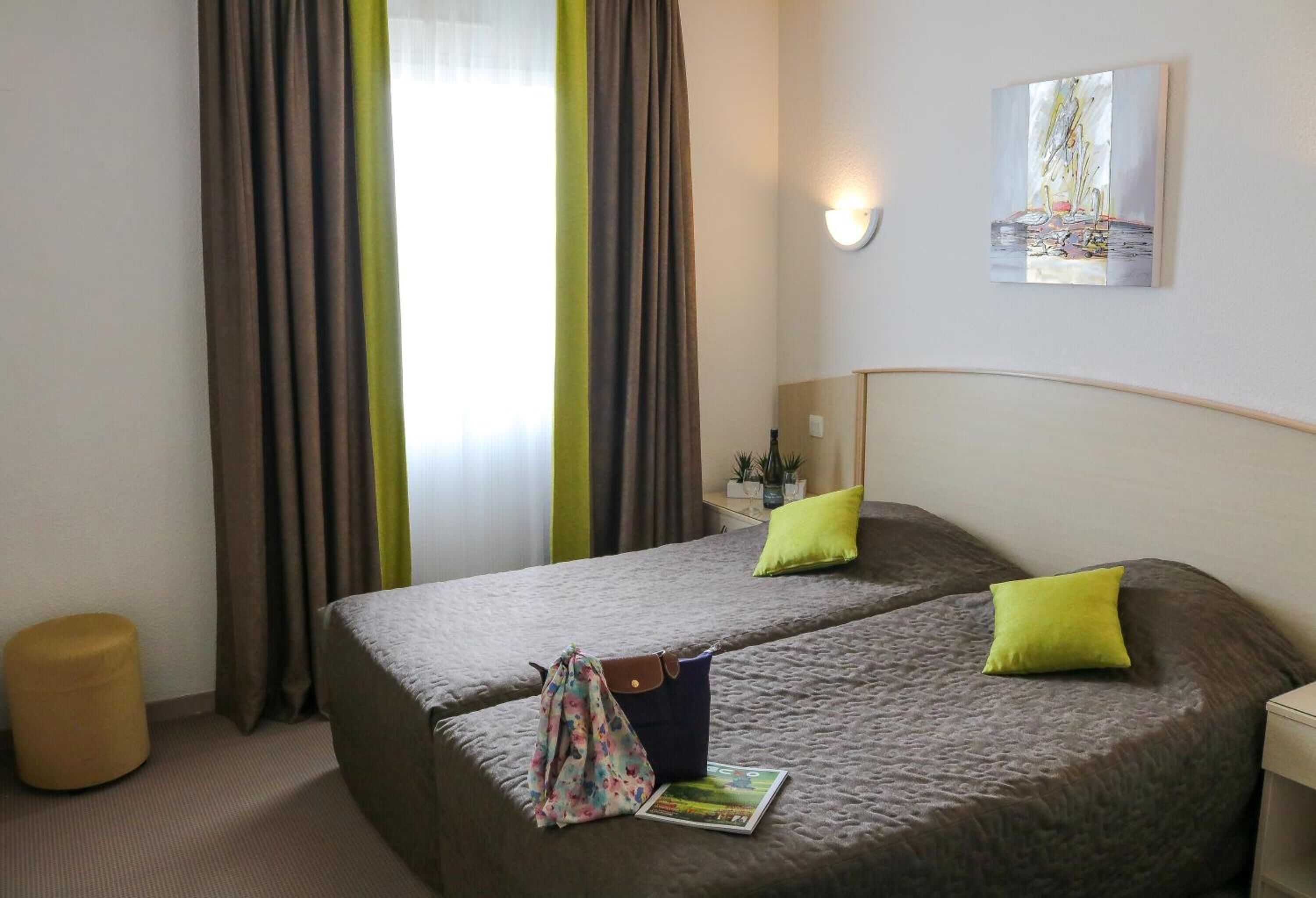 A hotel room with two beds, a small table, a lamp, and a painting on the wall.