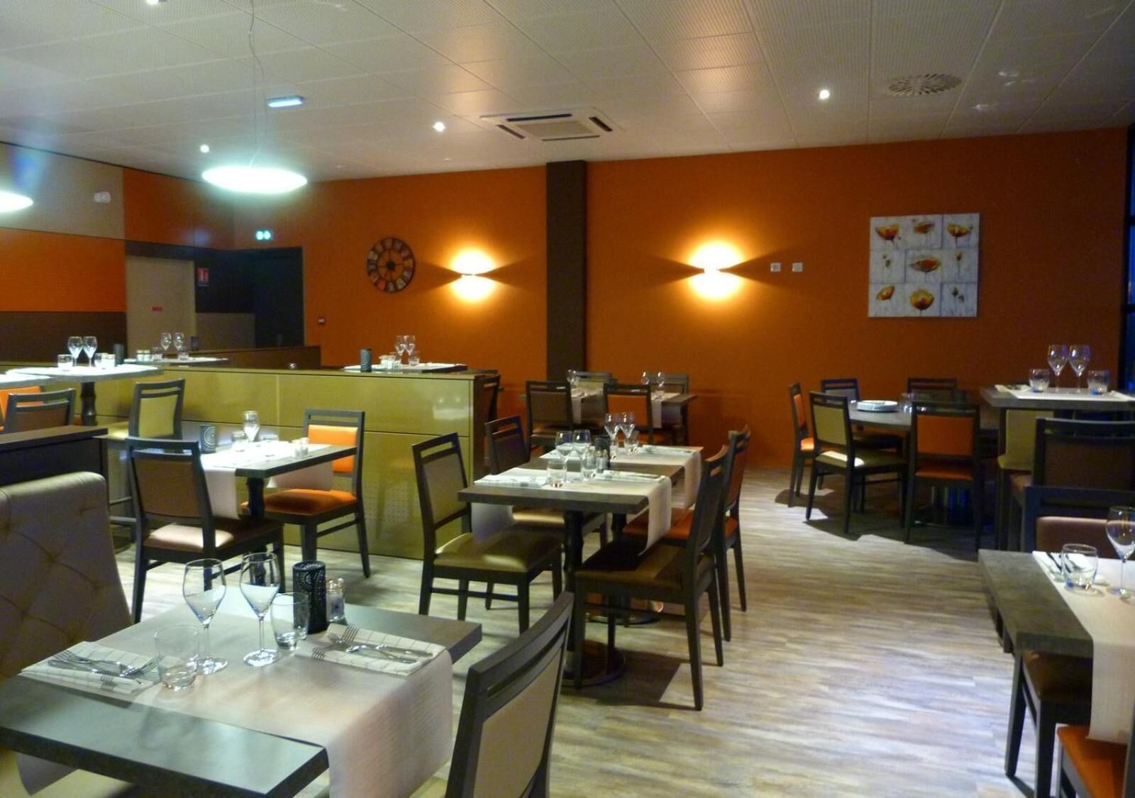 A restaurant with multiple tables and chairs, a central counter, and wall-mounted lighting.