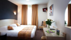 Une chambre d’hôtel équipée d’un lit, d’un bureau, d’une chaise, d’une télévision et d’une fenêtre avec des rideaux.