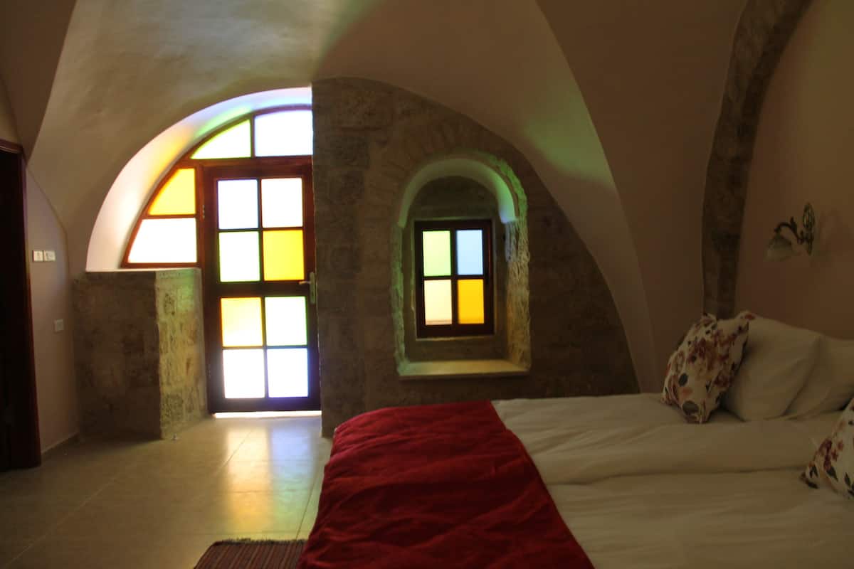 A bedroom with a large bed, a red blanket, and a small window with a view of the outside.