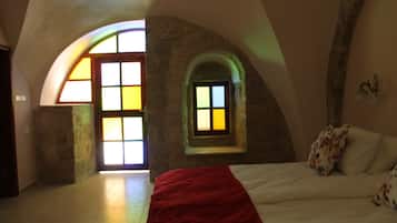 Une chambre à coucher avec un grand lit, une couverture rouge et une petite fenêtre donnant sur l’extérieur.
