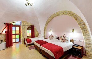 A bedroom with two beds, stone arches, a red curtain, and a stone wall. - Dar Sitti Aziza (Bethlehem)