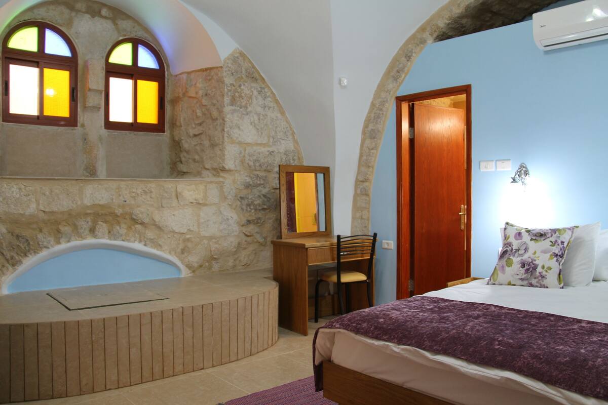 A bedroom with a stone wall, a wooden desk, a chair, a bed, and a door.