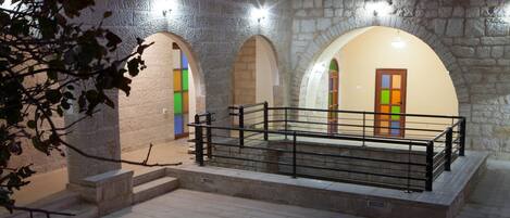 A stone-walled corridor with arched doorways, a staircase, and a railing.
