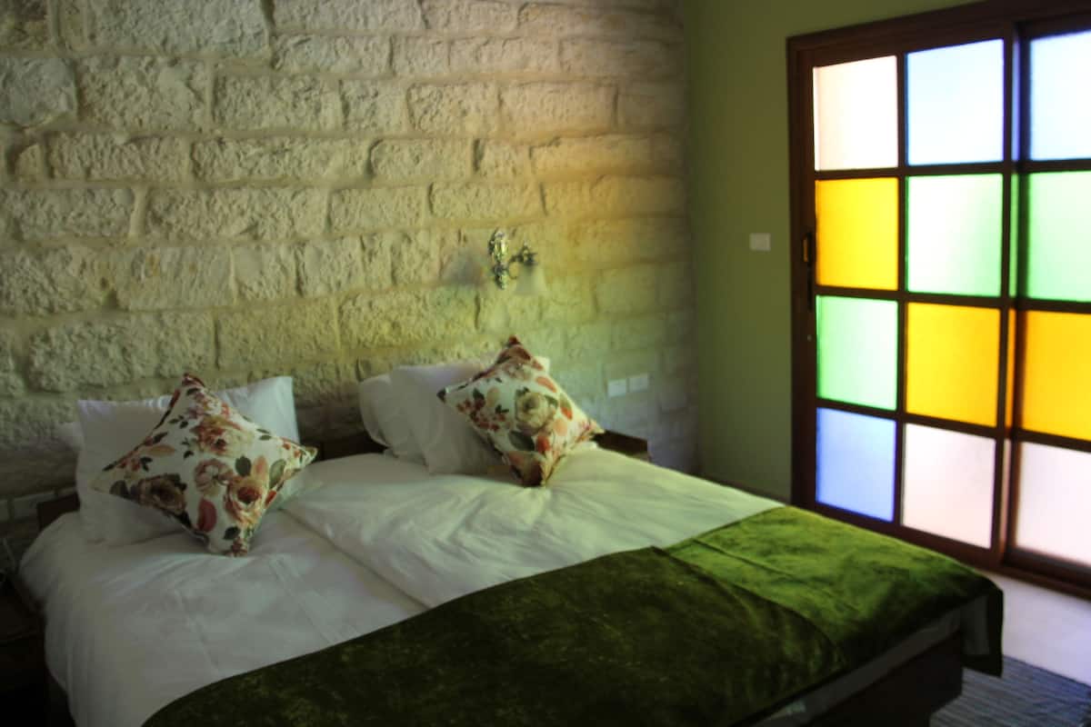 A bed with white linens and floral pillows, a green throw blanket, and a brick wall.