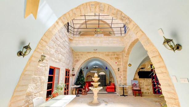 A spacious courtyard with stone arches, a central fountain, and a seating area with tables and chairs.
