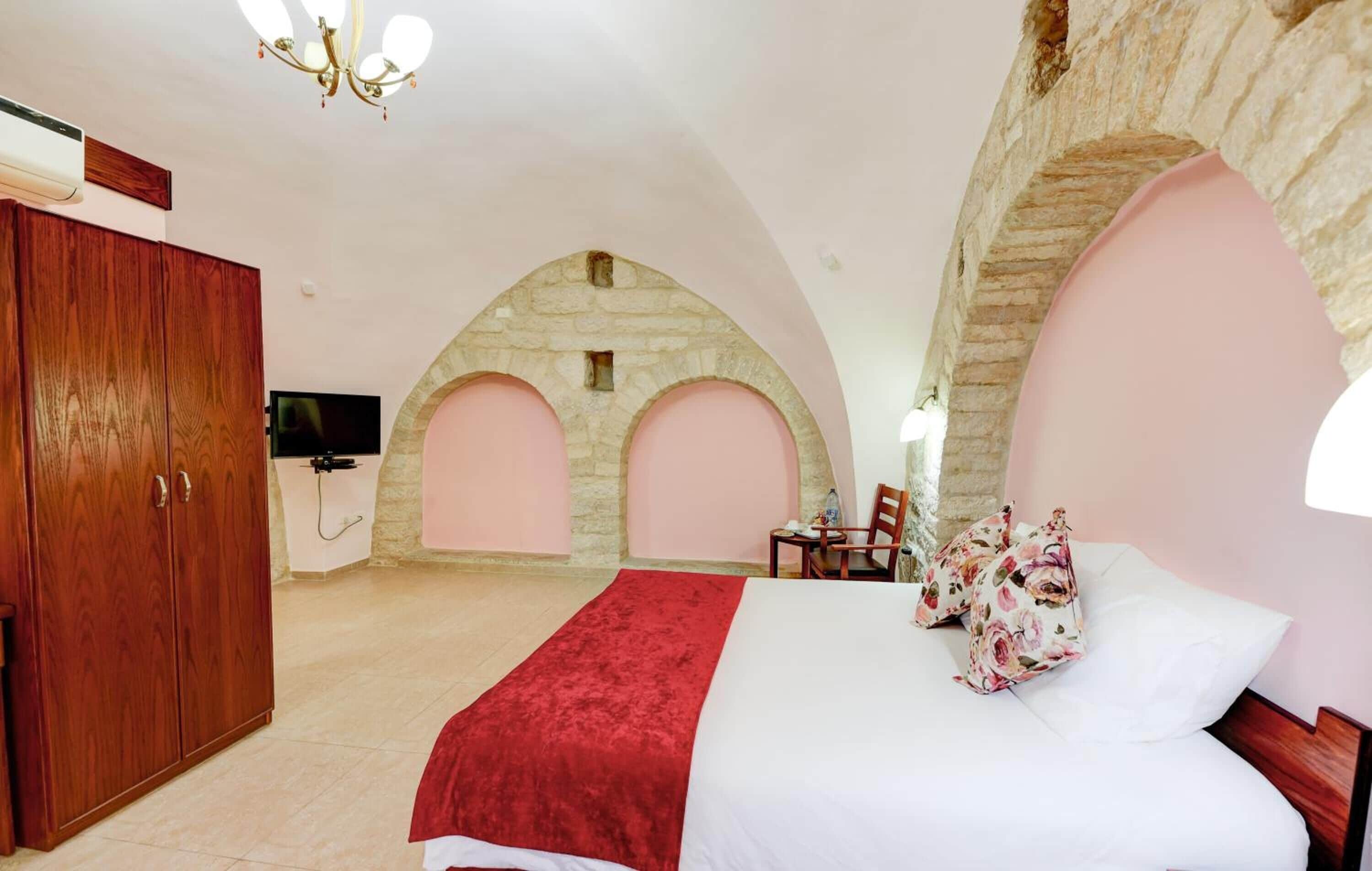 Un dormitorio con cama, armario de madera, televisor y arcos de piedra.