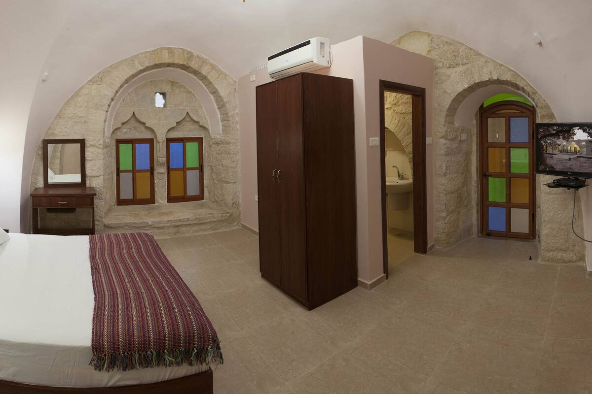 A bedroom with a bed, a nightstand, a dresser, and a TV. There are stone arches in the room.