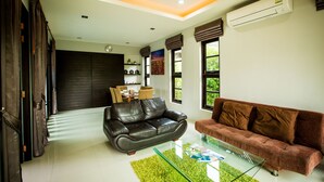 A modern living room with a glass coffee table, two sofas, and a dark-colored wall with a clock. - Buabaan Villa (Krabi)