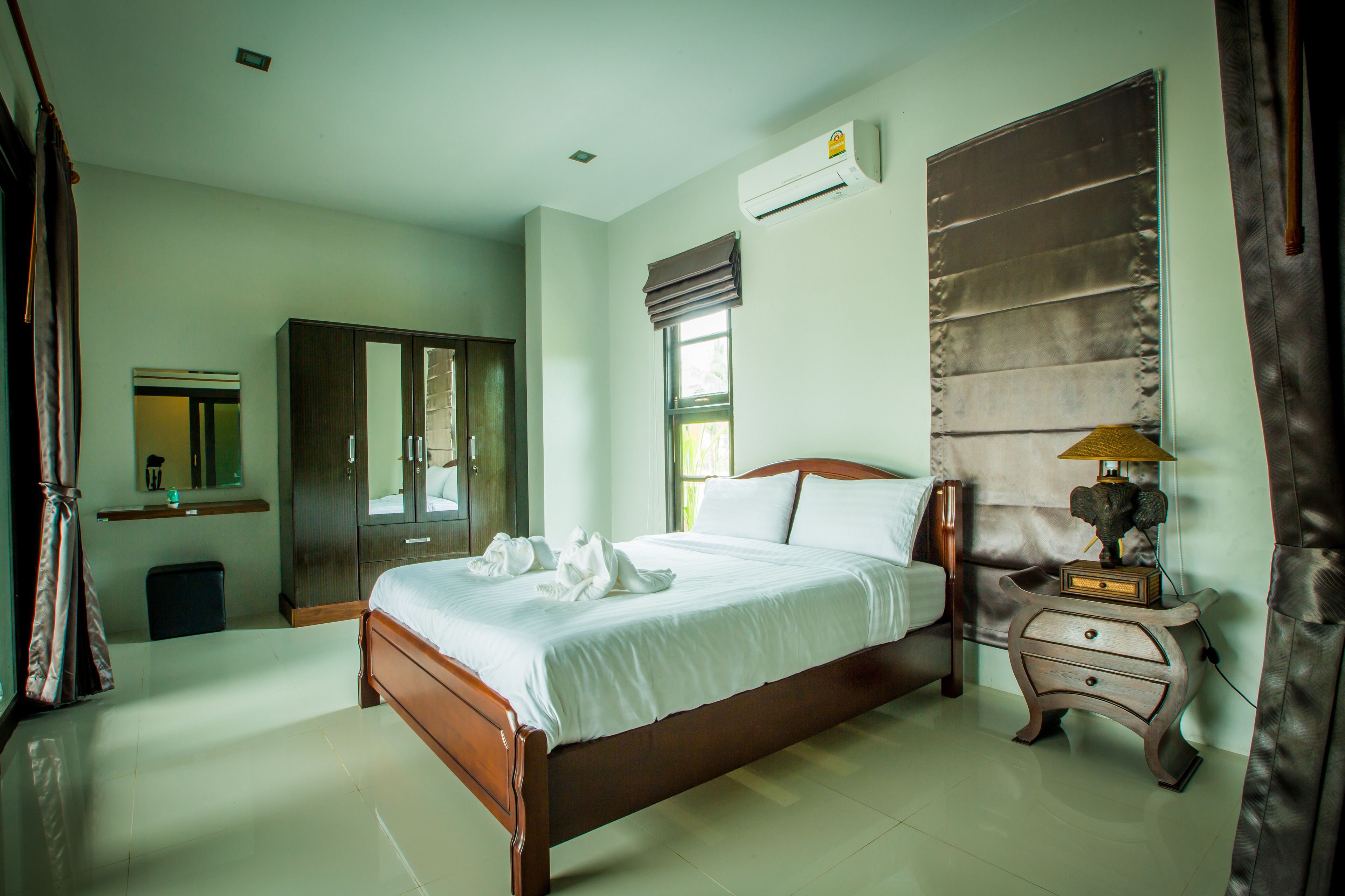 A bedroom with a wooden bed, a nightstand with a lamp, a wardrobe, and an air conditioning unit.
