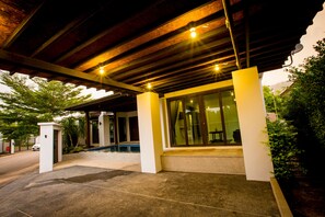 A covered outdoor area with a concrete floor, a wooden ceiling, and a glass door leading inside.