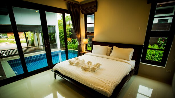 A hotel room with a large bed, a view of a swimming pool, and a television on the wall. - Buabaan Villa (Krabi)