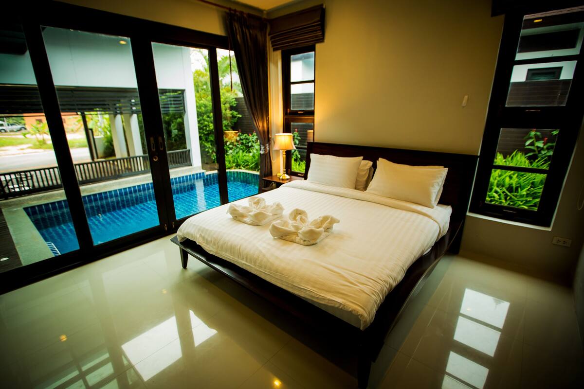A hotel room with a large bed, a view of a swimming pool, and a television on the wall.