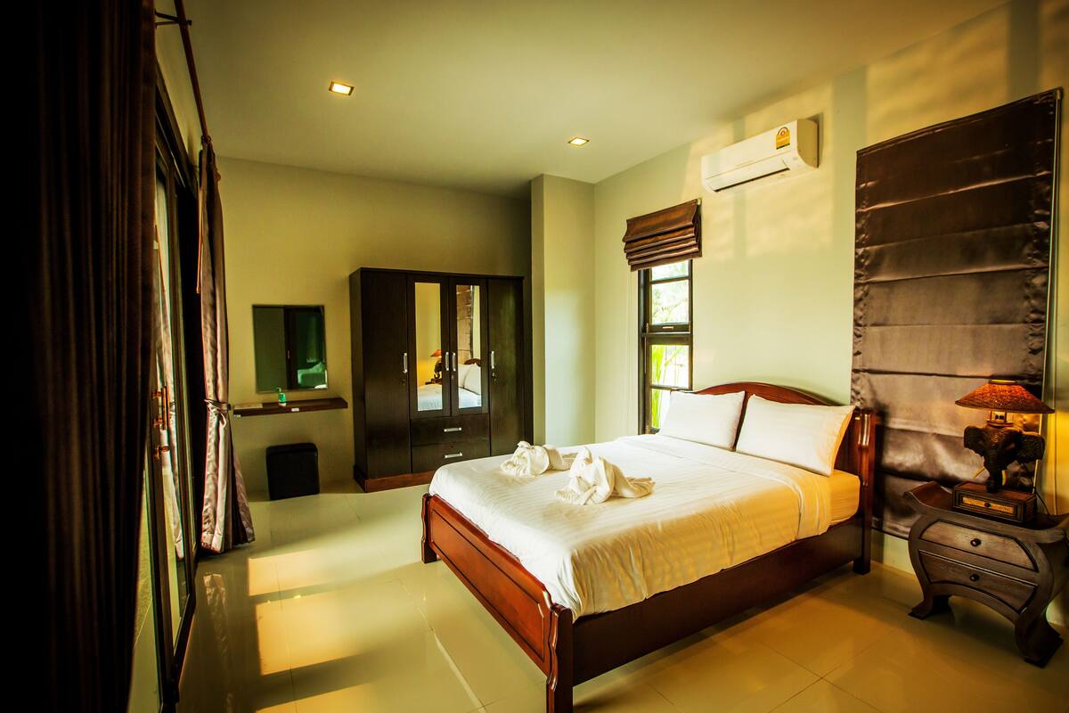 A hotel room with a large bed, a wardrobe, a bedside table with a lamp, and a window with curtains.