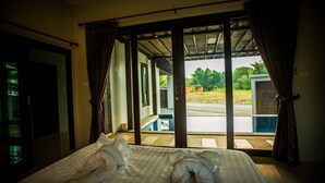 A hotel room with a bed, curtains, and a view of a swimming pool and greenery outside. - Buabaan Villa (Krabi)