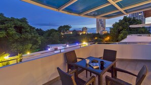 A rooftop terrace with a glass ceiling, wicker furniture, and a view of the cityscape at dusk. - Sharrow Bay (Pattaya)