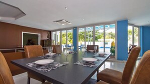 A dining area with a long table set for four, surrounded by brown leather chairs, with large windows offering a view of the outdoors. - Sharrow Bay (Pattaya)