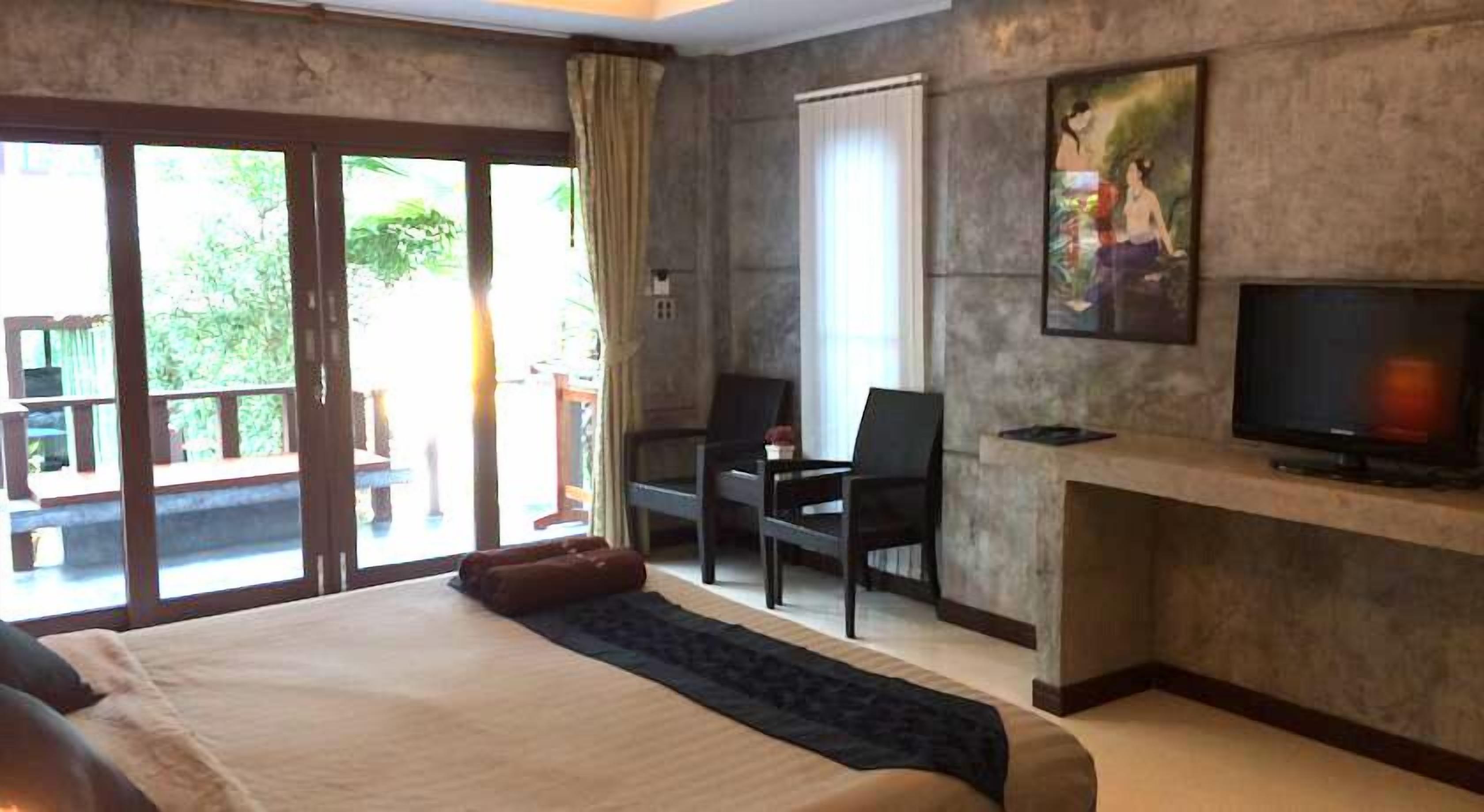 Habitación de hotel con una cama grande, televisión, escritorio con silla y puerta corrediza de vidrio que da a un área exterior.