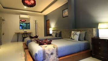 A bedroom with a large bed, a desk, and a chair. There is a window with a view of greenery.