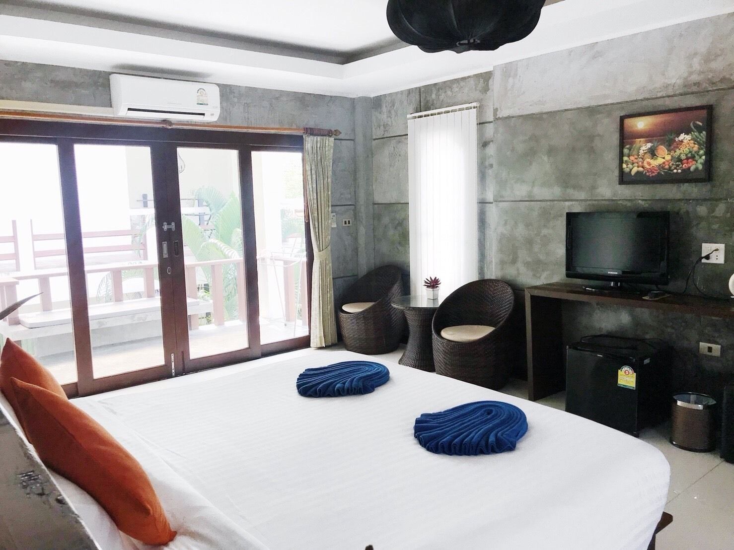 A hotel room with a bed, two chairs, a TV, and a painting on the wall.