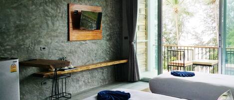 A hotel room with two beds, a TV mounted on the wall, a small desk with a chair, and a balcony with a railing.
