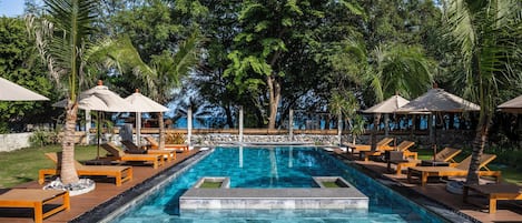 A pool area with lounge chairs and umbrellas, surrounded by trees and a view of the ocean.