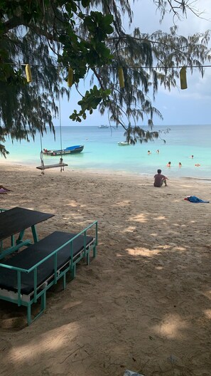 A beach with a swing set, a boat named "KOH 140 DIVERS" anchored nearby, and people swimming in the water.