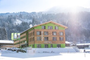 Un hotel con fachada verde y marrón, múltiples ventanales y un cartel que indica que es un hotel.