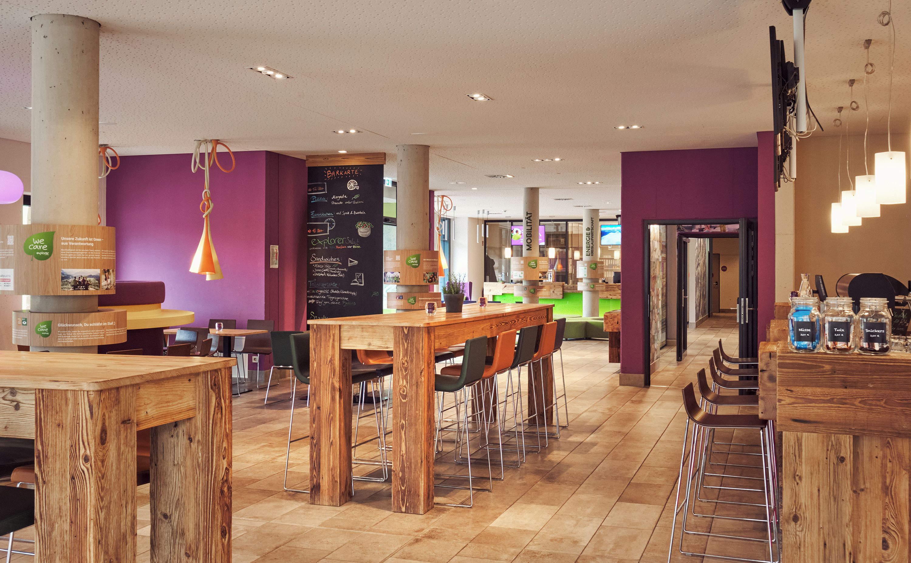 Un café moderno con mesas y sillas de madera, un menú en pizarra y una zona de mostrador verde.