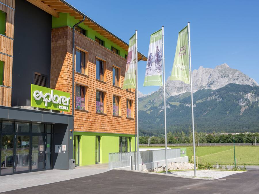 A modern building with a green and wooden facade, a visible storefront, and flags.