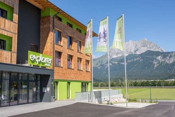 Un edificio moderno con fachada verde y de madera, un escaparate visible y banderas.