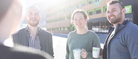 Three people standing outdoors, holding cups, with a modern building in the background.