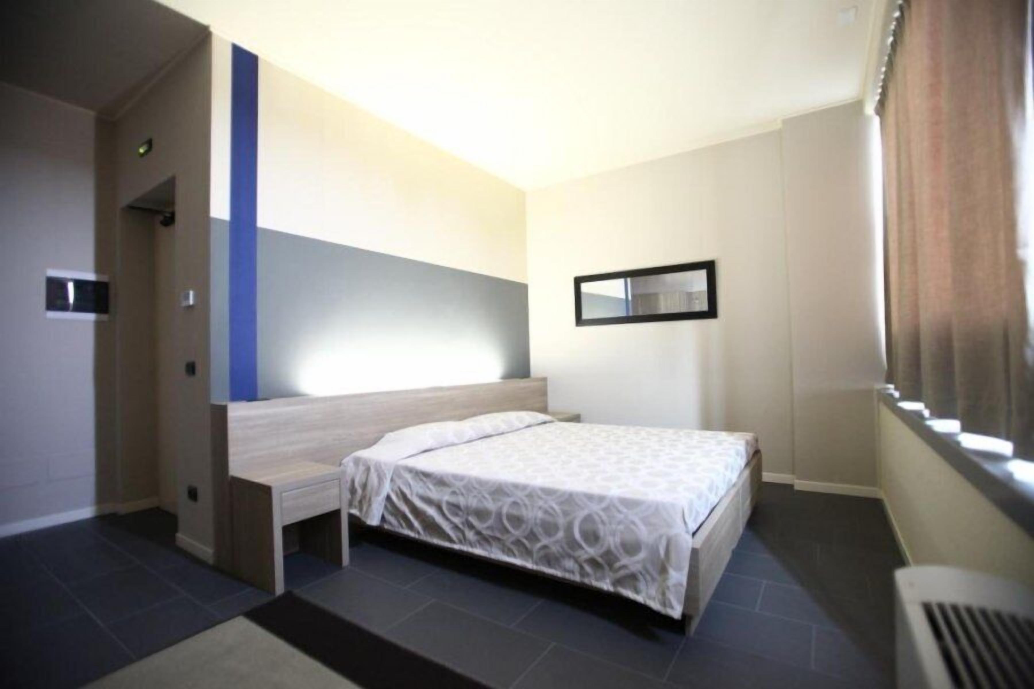 Una habitación de hotel con cama, mesita de noche, espejo y ventana con cortinas.