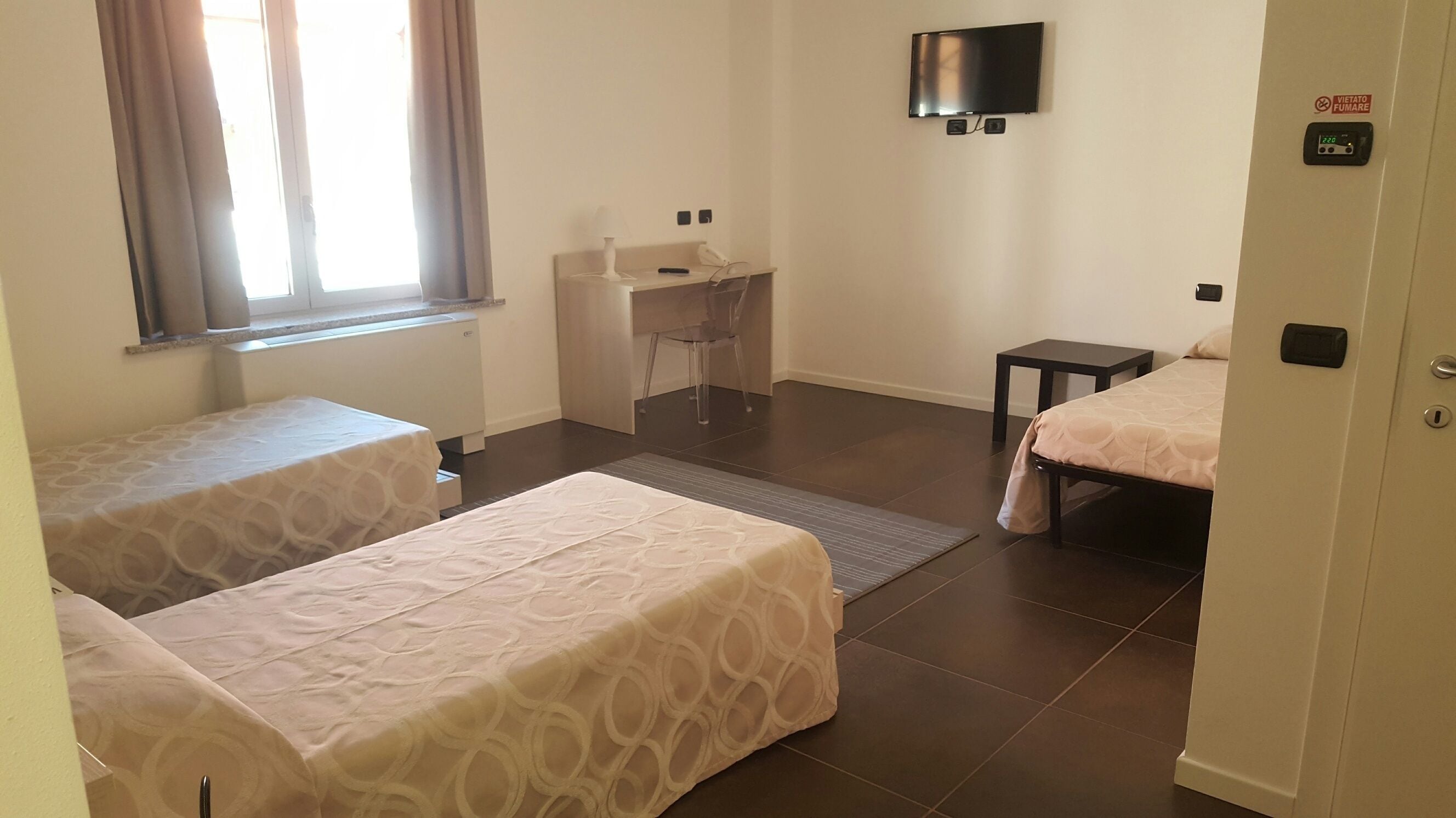 Una habitación de hotel con dos camas, un escritorio, una silla, un televisor y una ventana con cortinas.