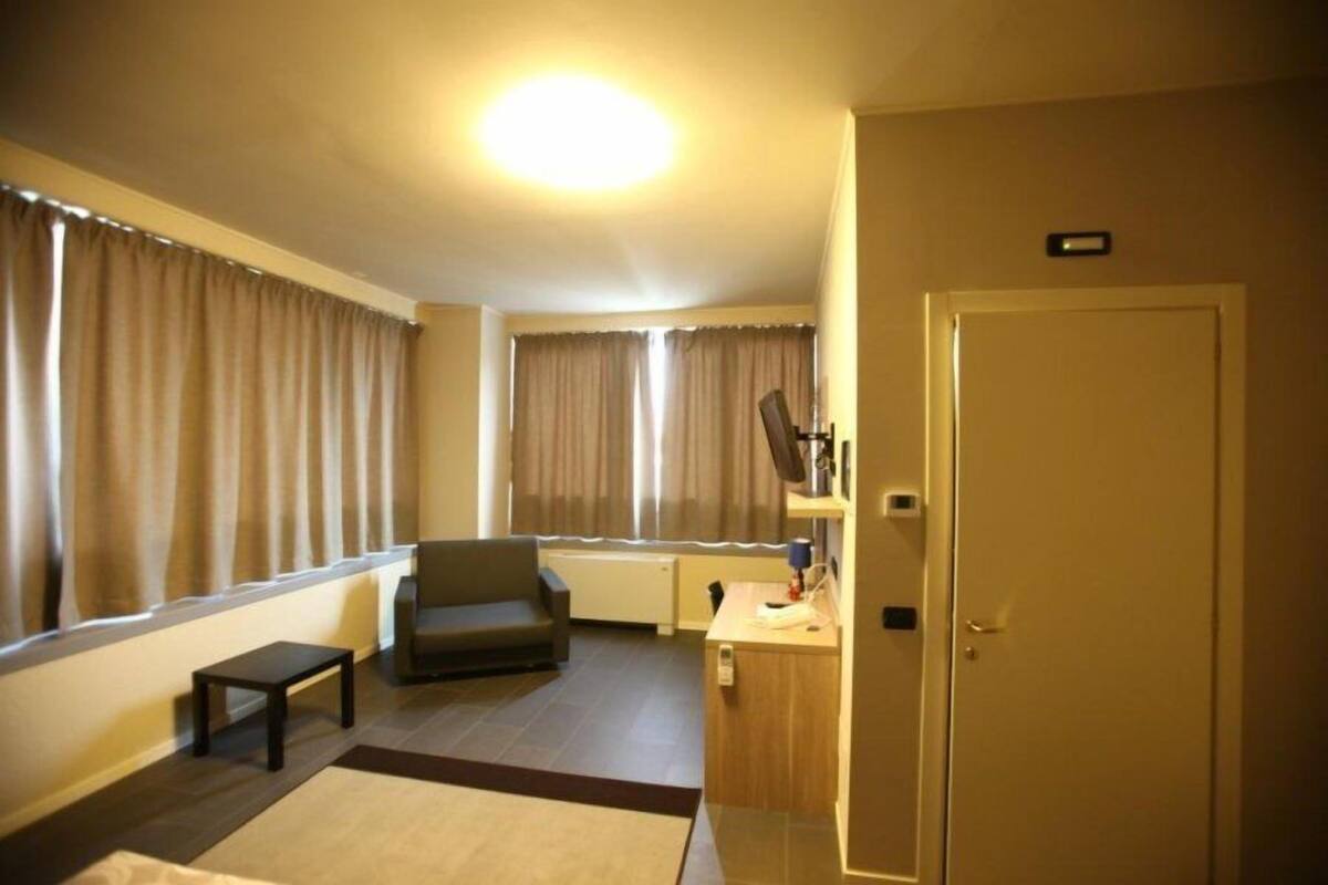 Une chambre d’hôtel avec un canapé, une petite table, un bureau avec une lampe et une porte.