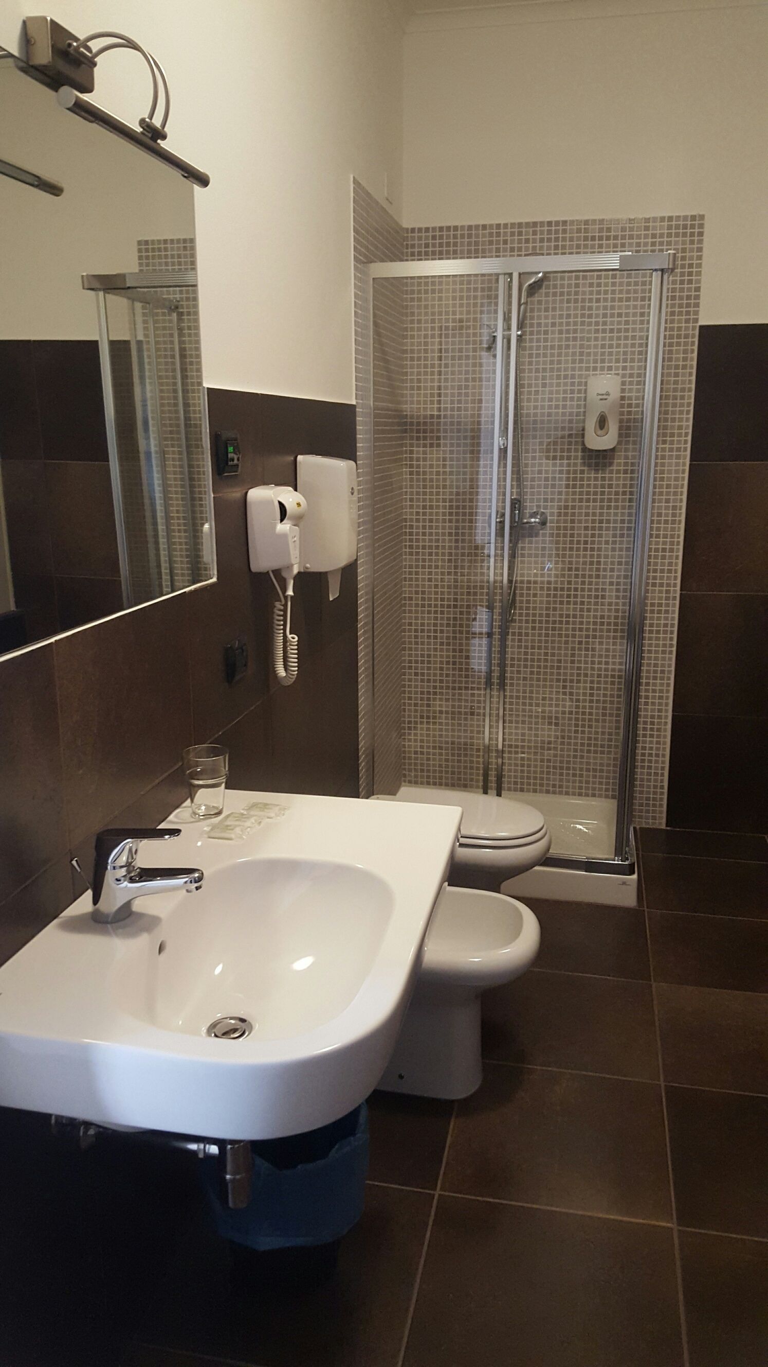 Et badeværelse med en hvid vask, toilet og en bruseniche med glasvægge.