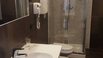 Et badeværelse med en hvid vask, toilet og en bruseniche med glasvægge.