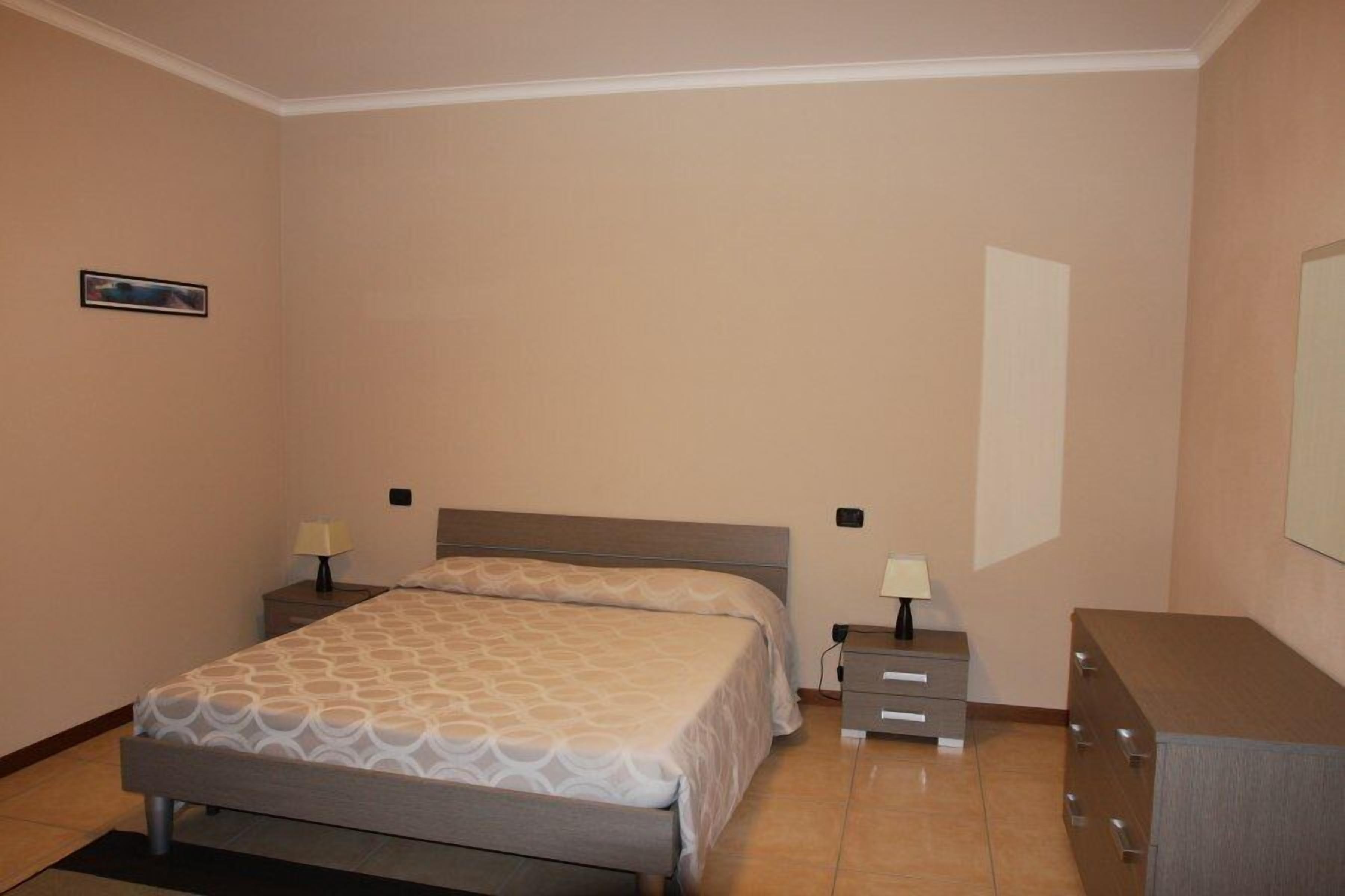 A bedroom with a bed, two bedside tables with lamps, a dresser, and a framed picture on the wall.