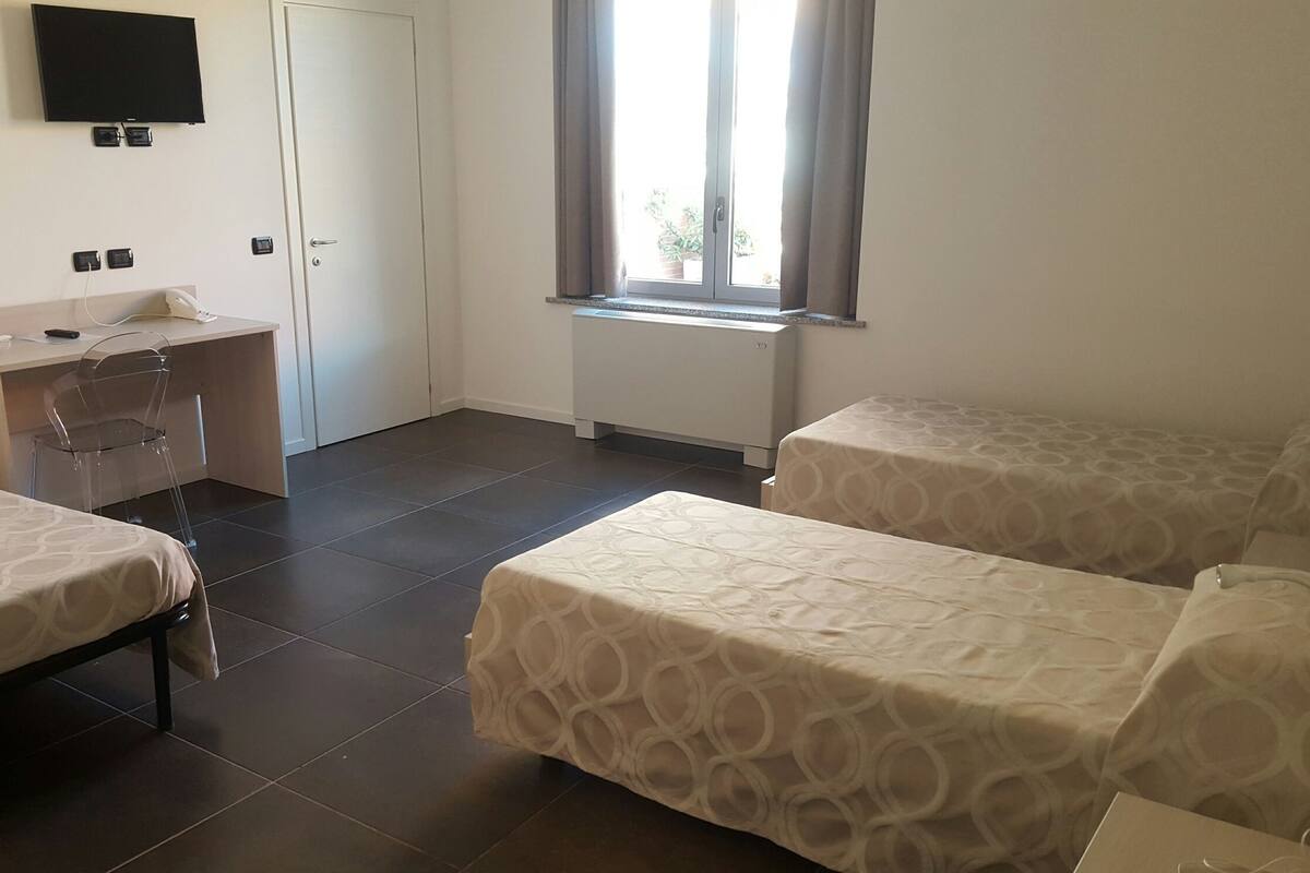 Une chambre d’hôtel avec deux lits, un bureau, une chaise, une télévision et une fenêtre avec des rideaux.