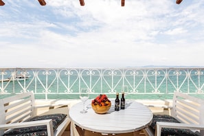 A round table with two chairs, a bowl of fruit, two wine bottles, and a wine glass on a balcony overlooking the sea. - Hotel Marabou (Kassandra)